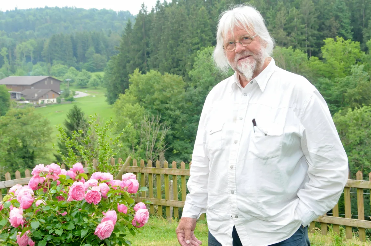 Man sieht Hans Denzler neben dem Rosenstrauch.